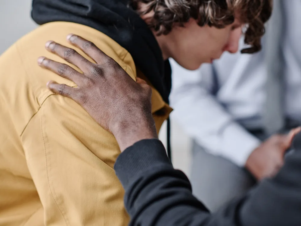 Une personne apporte son soutien à un jeune, une main posée sur son épaule